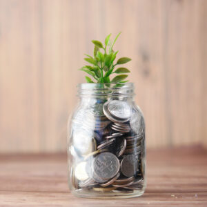 glass jar filled with coins has small leafy green plant growing out of it